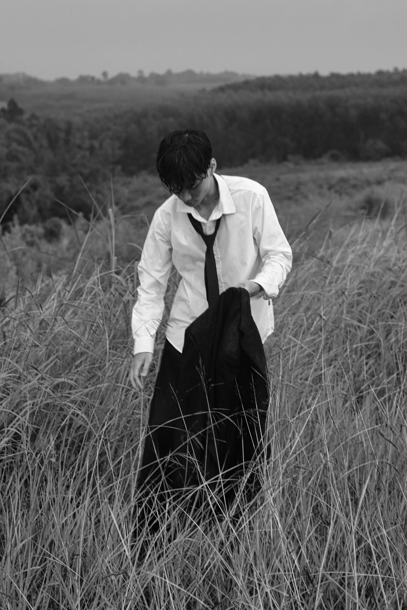 A well-dressed young man in a suit stands alone in a grassy field, conveying sophistication.